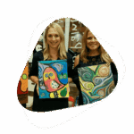 Two women holding up paintings in front of a mirror.