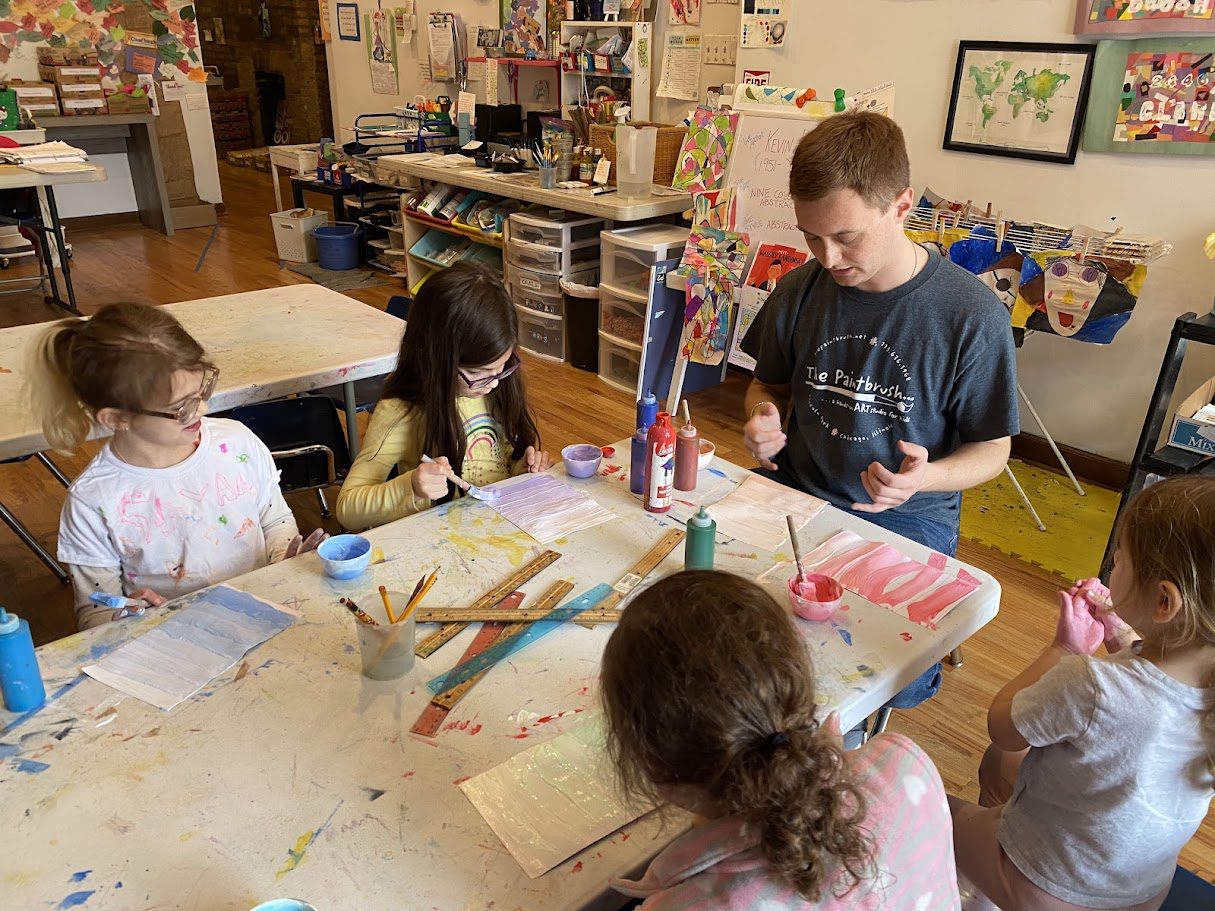 A group of children sitting at a table with paint.